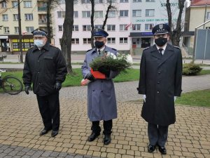 Trzech mężczyzn w mundurach, po środku stoi policjant, który trzyma wiązankę kwiatów.