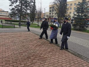trzech mężczyzn w mundurach udaje się po pomnik, po środku znajduje się policjant, który trzyma wiązankę kwiatów.