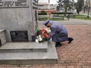 Policjant w mundurze składa wiązankę z kwiatami pod pomnikiem.